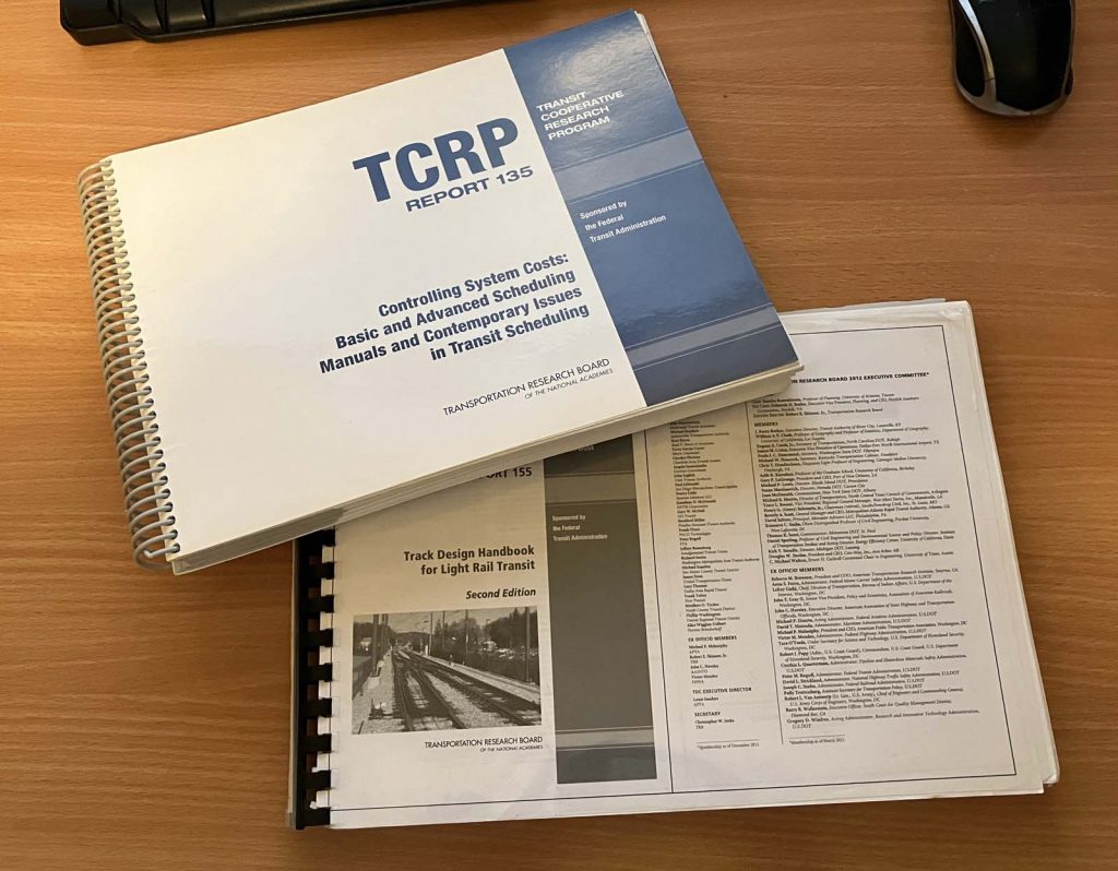 Picture of two TCRP reports on a desktop. The reports are TCRP Report 135 "Controlling system costs: basic and advanced scheduling manuals and contemporary issues in transit scheduling" and TCRP Report 155 "Track design handbook for light rail transit, second edition"