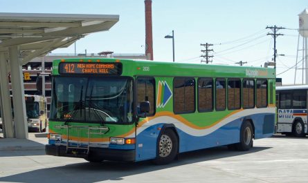 A modern single-decker American bus, in a predominantly green and blue livery, belonging to Triangle Transit, on a route 412 service to New Hope Commons and Chapel Hill. The bus is in an American urban transit center with an urban landscape beyond.