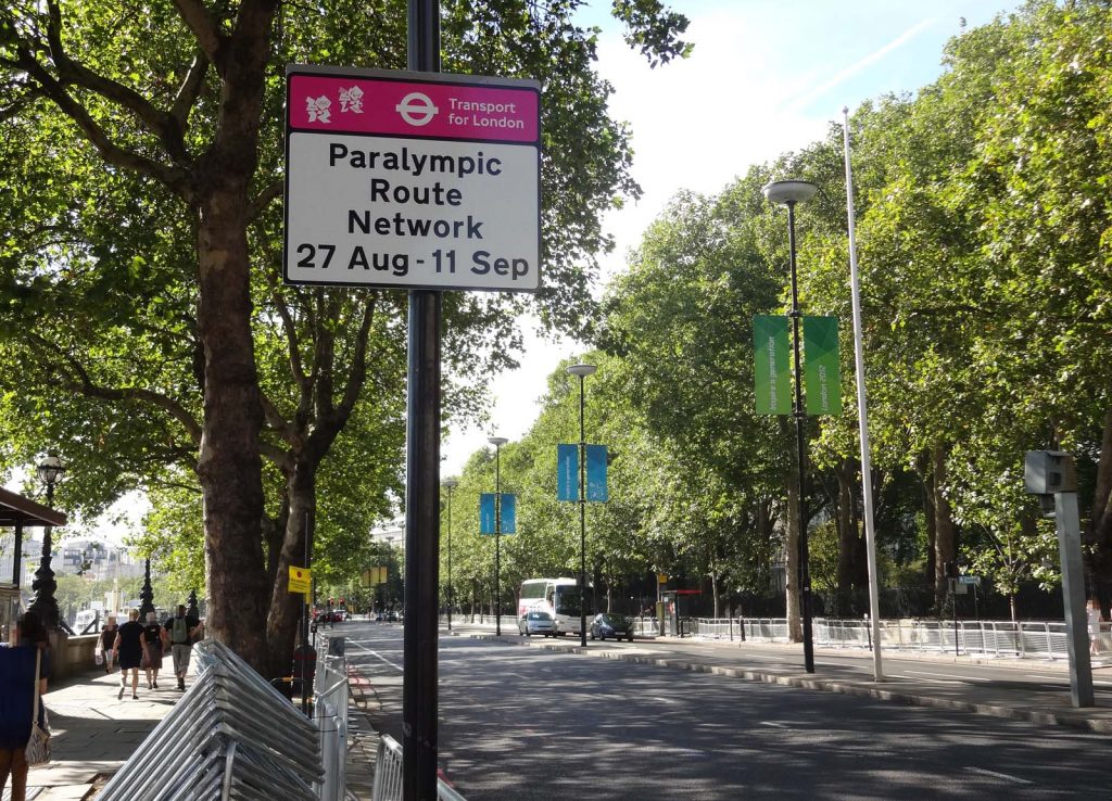 The Embankment (a main road) in central London.. A sign states that this is part of the Paralympic Route Network from 27 August to 11 September. The street is decorated with London 2012 banners hanging from the street lamps. There are temporary crowd barriers, but no crowds. Traffic is light.