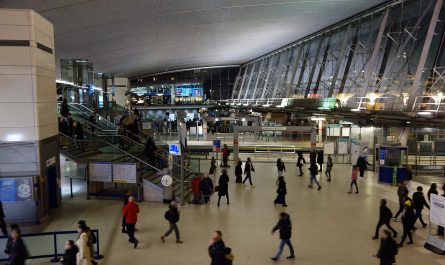 Photo inside the main ticket hall of Stratford station, after dark, looking from the first floor at one end, over the Jubilee line concourse and across the DLR platforms towards the main gateline at the other end. The ticket hall is busy with people.