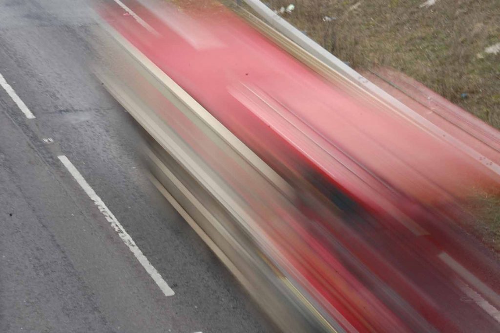 Photo looking down on a road, with a blurred large red-and-white vehicle going past at speed