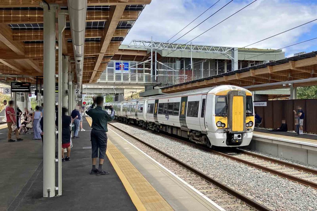 Photo at platform level at Cambridge South. A Great Northern train of class 387 units is arrriving at platform 1. Several enthusiasts are watching and taking photos or videos. Other passengers are waiting for a train.